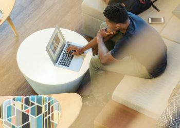 man using gray laptop while sitting on beige sofa