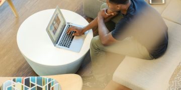 man using gray laptop while sitting on beige sofa