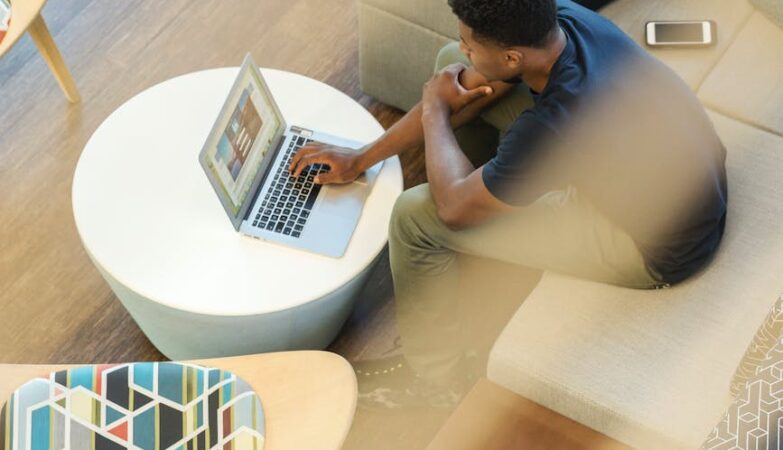 man using gray laptop while sitting on beige sofa